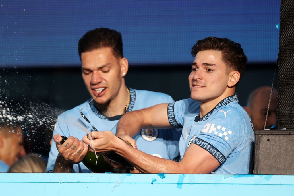 Ederson and Julian Alvarez of Manchester City spray fans of Manchester City with champagne as they celebrate during the Manchester City trophy para...
