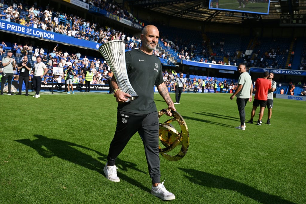 Chelsea boss Enzo Maresca carries the Conference League and Club World Cup trophies on the pitch at Stamford Bridge.