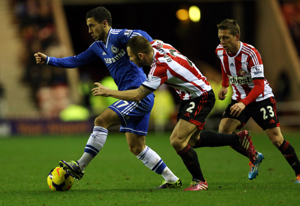 Chelsea star Eden Hazard dribbling away from Sunderland players in a Premier League match.