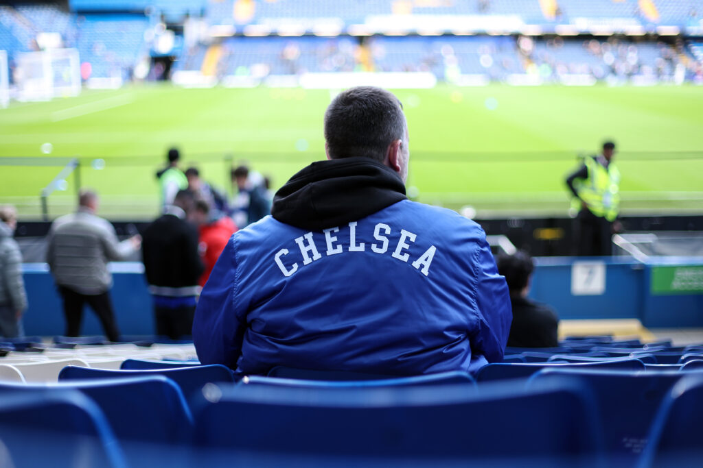 A fan wears a Chelsea jacket with has back to the camera at Stamford Bridge