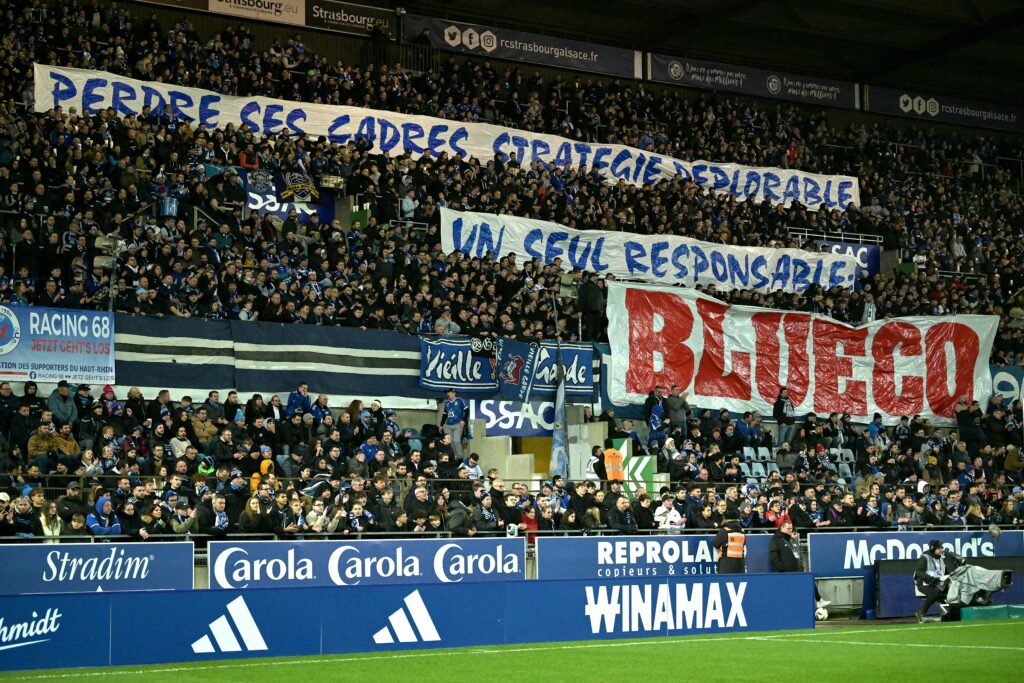 Strasbourg's supporters hold banners hostile to the new owner of the club reading "Losing executives, deplorable strategy - Only one person to blame, Blueco" during the French L1 football match between RC Strasbourg Alsace and stade Brestois 29 at the Stade de la Meinau in Strasbourg, eastern France, on February 24, 2024.